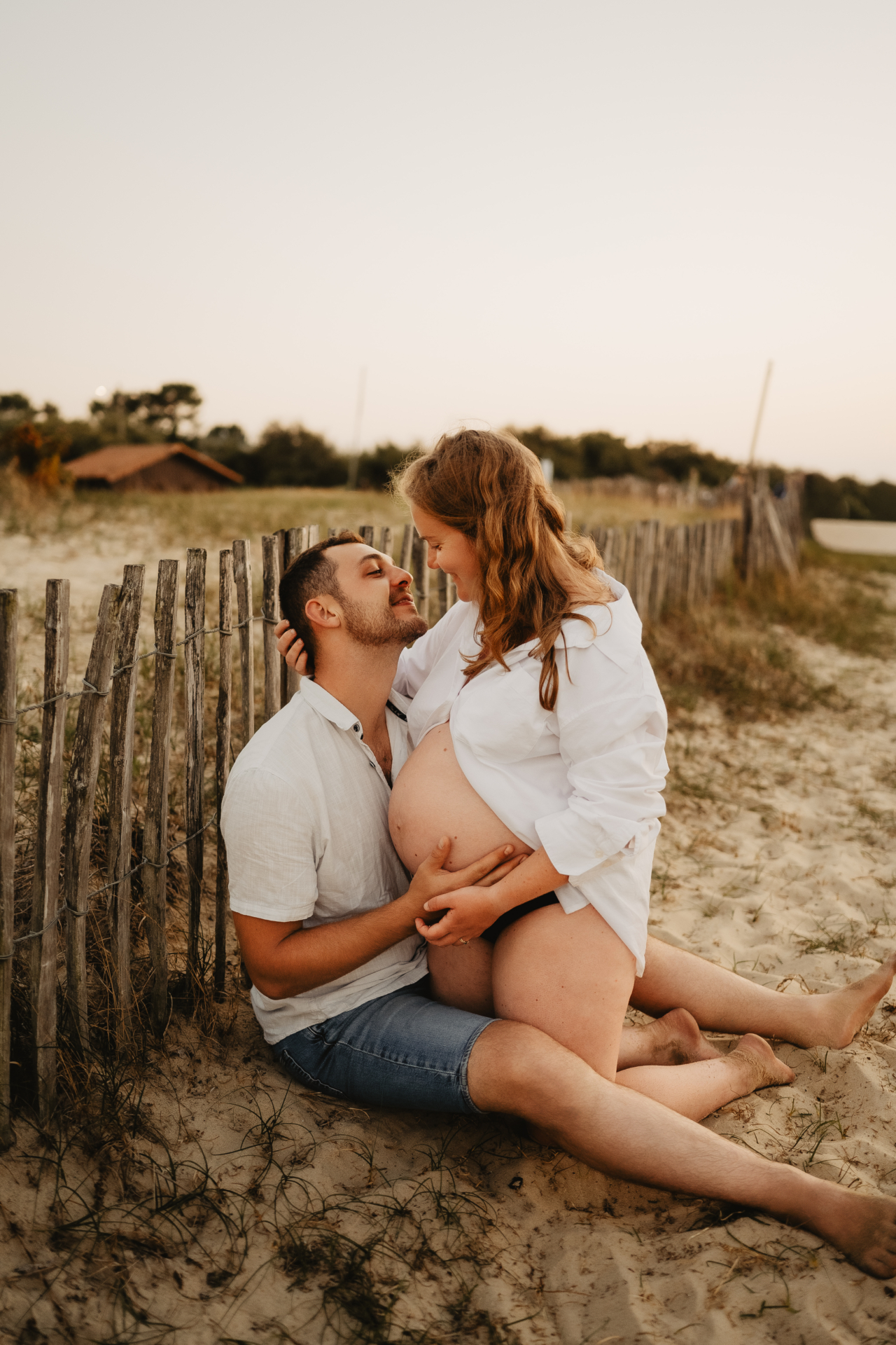 Future maman assise dans l'herbe haute au soleil couchant